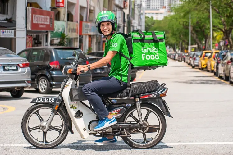 Grab rider malay male on motorbike wearing green helmet and green carrier bag