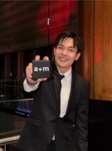 Paperballad&Co. CEO in a black tuxedo smiles while holding an award toward the camera at an industry event, representing the achievement of a creative agency in Malaysia through strategic excellence and award winning leadership.